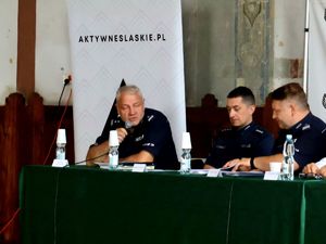 na zdjęciu zastępca komendanta przemawia do mikrofonu, obok mundurowi, siedzą przy stole