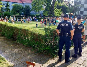 na zdjęciu policjant i policjantka stoją tyłem, przed nimi osoby zgromadzone na placu zabaw.