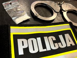 na zdjęciu woreczek foliowy z białym proszkiem, kajdanki i opaska z napisem Policja