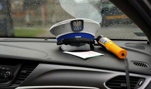 na zdjęciu policyjna czapka, urządzenie do badania trzeźwości leżą na podszybiu w radiowozie