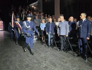 Na zdjęciu stojący w teatrze mundurowi i goście. Obok nich trzech idących ze sztandarem policjantów.