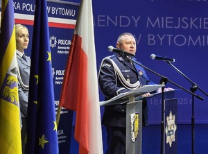 na zdjęciu bytomski komendant przy mównicy, obok flagi Polski, Unii Europejskiej i Bytomia