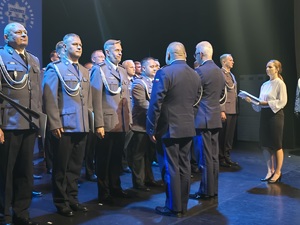 stojący na scenie mundurowi w trakcie gratulacji od komendanta wojewódzkiego i miejskiego