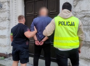 na zdjęciu zatrzymany w kajdankach prowadzony przez dwóch nieumundurowanych policjantów