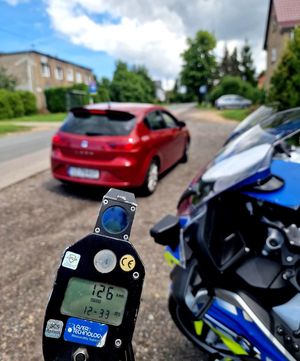 na zdjęciu urządzenie pomiarowe, wynik 126, obok policyjny motocykl i czerwony seat