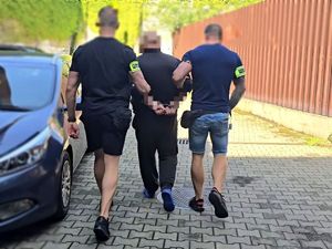 na zdjęciu mężczyzna w kajdankach, prowadzony przez nieumundurowanych policjantów