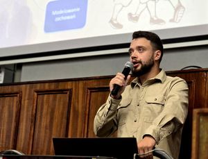 na zdjęciu policyjny psycholog w trakcie przemowy, trzyma mikrofon przy ustach