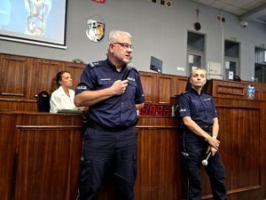 na zdjęciu zastępca komendanta w trakcie przemowy, trzyma mikrofon przy ustach przy nim policjantka