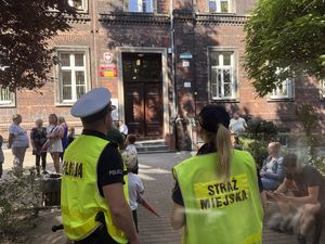 na zdjęciu policjant i strażniczka miejska przy budynku szkoły