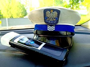 na zdjęciu leżąca na podszybiu w aucie policyjna czapka i urządzenie do badania trzeźwości