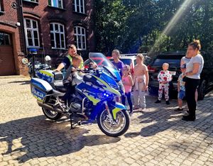 na zdjęciu policjant, obok dziecko na motocyklu służbowym, obok dzieci i dwie kobiety