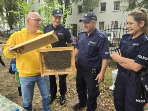 na zdjęciu mężczyzna trzyma w drewnianym pudełku pszczoły obok dwóch policjantów i policjantka