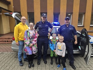 na zdjęciu radiowóz policyjny, przy nim dwóch policjantów i zgromadzone osoby