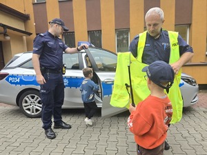 na zdjęciu radiowóz policyjny, przy nim dwóch policjantów i dwóch chłopców, jeden w policyjnej czapce
