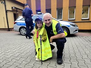 na zdjęciu policjant przy małym chłopcu ubranym w żółtą kamizelkę policyjną, za nimi policjant i radiowóz