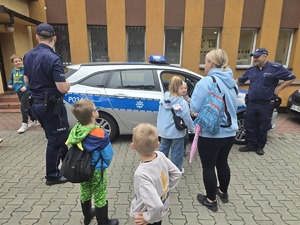 na zdjęciu radiowóz policyjny, przy nim dwóch policjantów i zgromadzone osoby