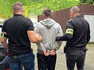 na zdjęciu zatrzymany mężczyzna prowadzony przez dwóch nieumundurowanych policjantów
