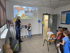 na zdjęciu policjantka, obok chłopiec i dzieci siedzące na krzesłach