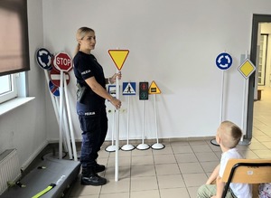 na zdjęciu policjantka, obok znaki drogowe, w dłoni trzyma znak ustąp pierwszeństwa