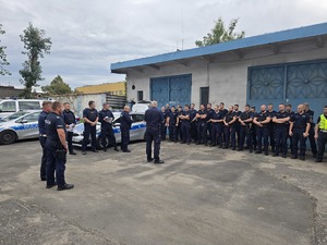 na zdjęciu policjanci stojący w rzędzie przednimi kilku policjantów ,obok radiowozy