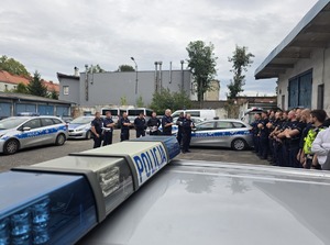 na zdjęciu policjanci stojący w rzędzie przednimi kilku policjantów ,obok radiowozy