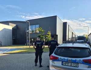 na zdjęciu dwóch policjantów przy radiowozie, stoją przed lodowiskiem