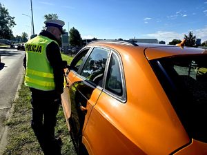 na zdjęciu policjant ruchu drogowego stojący przy pomarańczowym samochodzie