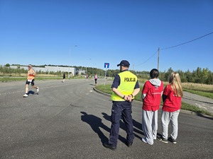 na zdjęciu policjant w kamizelce odblaskowej i dwie wolontariuszki w czerwonych bluzkach