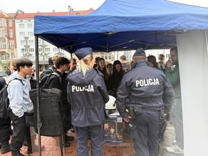 policjant i policjantka przy stoisku profilaktycznym przy nich zgromadzone osoby