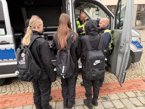 na zdjęciu dwóch policjantów i radiowóz policyjny, przy nim uczniowie klas mundurowych