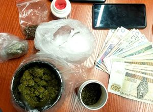 na zdjęciu leżące na stole narkotyki, w okrągłym pudełku czerwone tabletki, w dwóch okrągłych pudełkach i w dwóch workach susz brunatnozielony, w worku biały proszek, obok leżą banknoty i telefon
