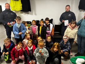 na zdjęciu w budynku dzieci ustawione do zdjęcia pomiędzy dwoma policjantami, którzy trzymają obrazki narysowane przez dzieci