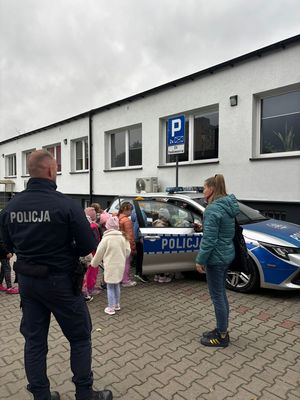 na zdjęciu przed komisariatem dzieci wchodzą do radiowozu, obok policjant