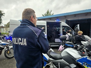 na zdjęciu na zewnątrz budynku policjant , obok pojazdy służbowe, motocykle służbowe i uczniowie klasy mundurowej
