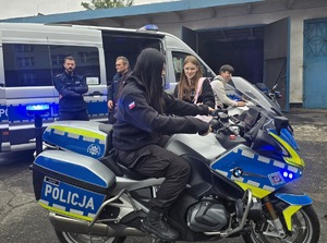 na zdjęciu dziewczyna na motocyklu służbowym, obok radiowóz policjanci i uczniowie