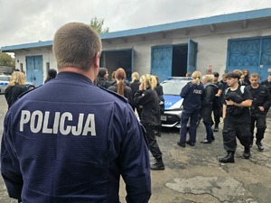 na zdjęciu policjant, przed nim licealiści przy radiowozie służbowym