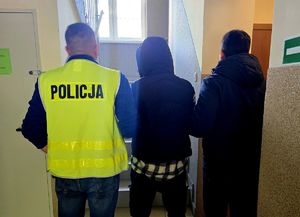 na zdjęciu dwóch nieumundurowanych policjantów trzymają zatrzymanego mężczyznę za ramiona