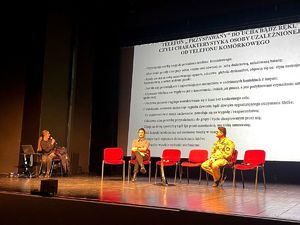 na zdjęciu na scenie trzy osoby prowadzące debatę, za nimi wyświetlony slajd dotyczący uzależnień
