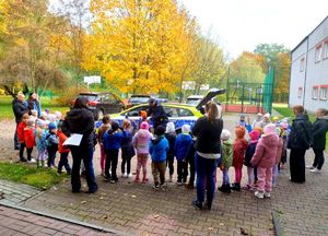 na zdjęciu policjant pośród przedszkolaków i opiekunów , przy radiowozie służbowym