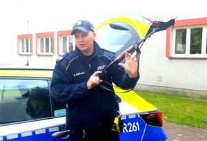 na zdjęciu policjant przy radiowozie, trzyma w dłoni broń