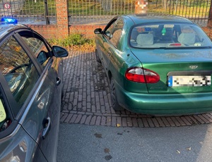 na zdjęciu zielony samochód obok fragment nieoznakowanego radiowozu