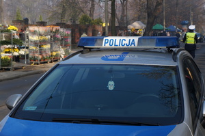 na zdjęciu radiowóz, za nim policjant obok cmentarza