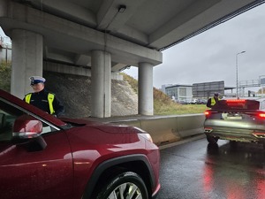 na zdjęciu policjanci na jezdni obok pojazdów, badają trzeźwość kierujących