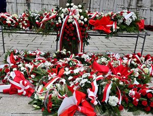 na zdjęciu wiązanki kwiatów biało czerwonego koloru złożone przed pomnikiem Wolności