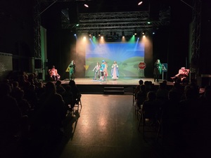 młodzi aktorzy jeżdżą na hulajnogach i tańczą na scenie w trakcie przedstawienia, przed nimi widownia