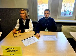 przy stole kobieta i policjant, na stole kartka na niej napis zespół ewidencyjno kadrowy