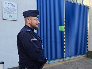 na zdjęciu policjant stojący przed bramą wjazdową jednostki