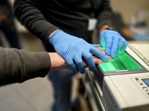 pobieranie śladów odcisków palców, widoczne urządzenie daktyloskopijne i dłonie w niebieskich rękawiczkach na dłoni mężczyzny