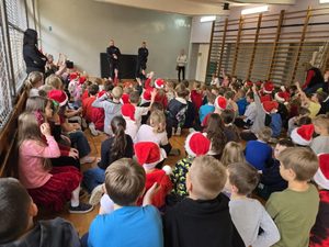 na zdjęciu dwóch policjantów przez nimi dzieci w czapkach mikołajowych