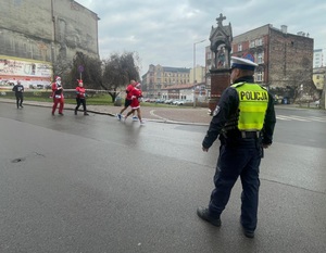 na zdjęciu policjant, obok ludzie biegnący w mikołajowych strojach
